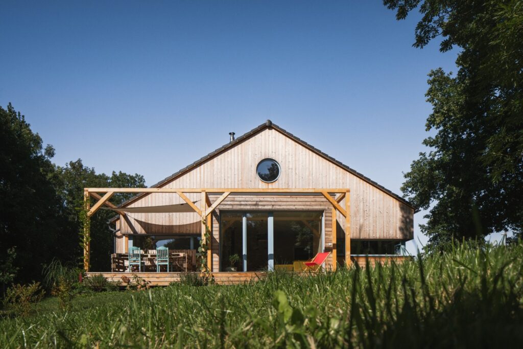 CLT dřevostavba s dřevěnou fasádou, prosklenou stěnou a krytou terasou ve svahu