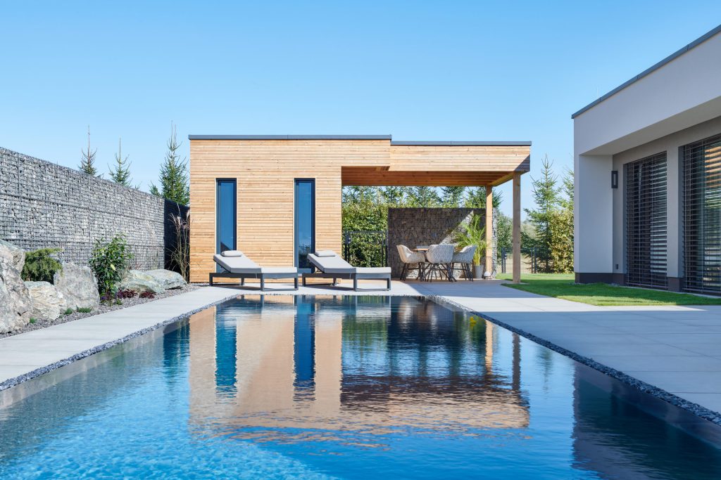 Dřevěný zahradní domek s pergolou a lehátky u bazénu