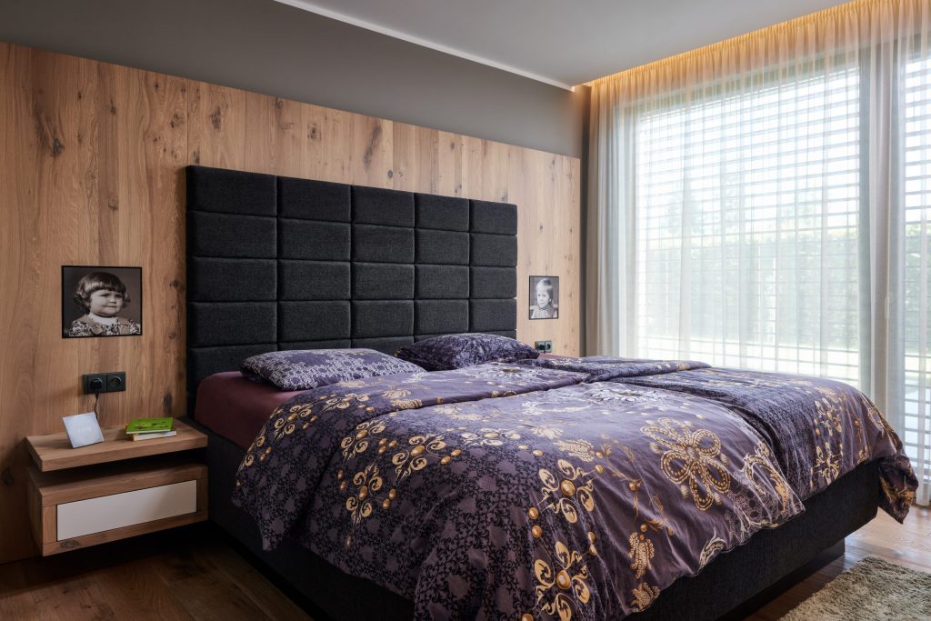 Ložnice s čalouněným čelem postele a dřevěnou obkladovou stěnou