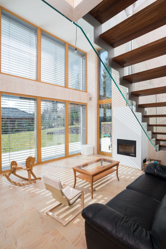 Obývací pokoj s vysokým stropem, krbem, schody a velkými okny