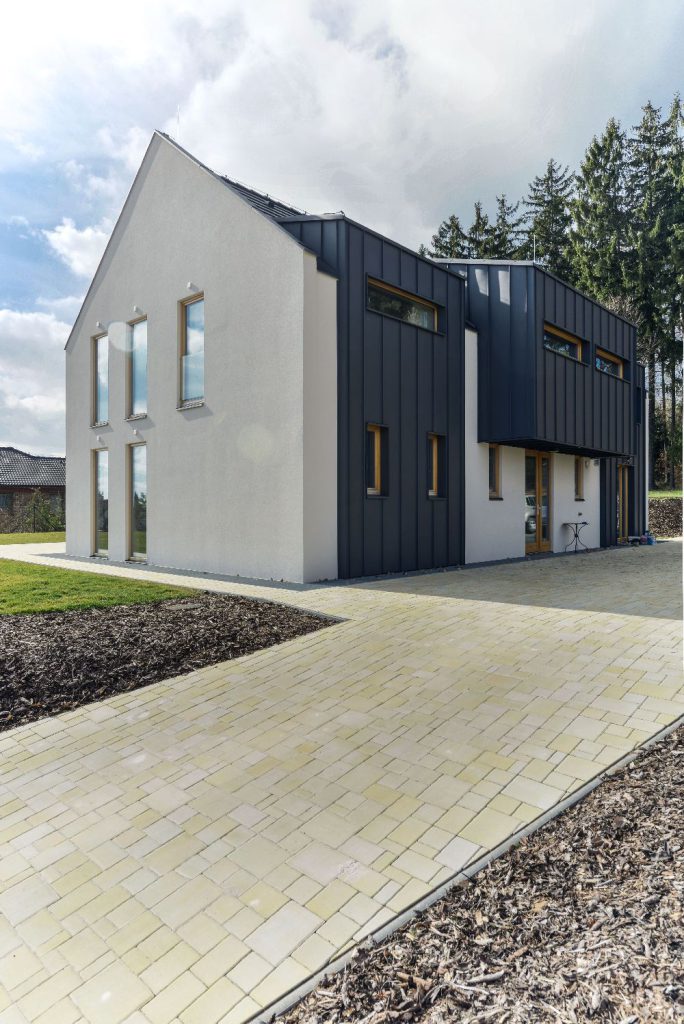 Moderní dřevostavba realizovaná firmou 3AE s kombinací bílé omítky a tmavého obkladu na kraji lesa