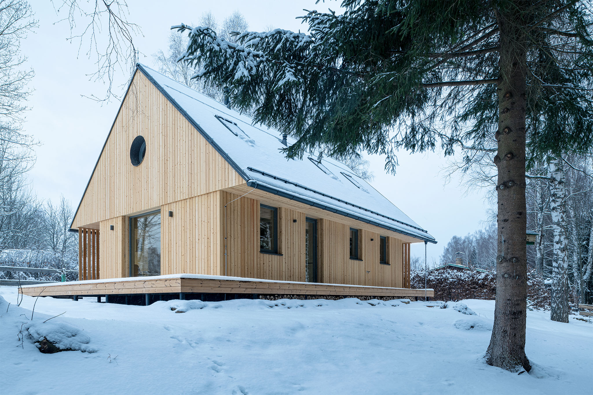 Jezerní chata Lipno je dřevostavba z CLT panelů s dřevěnou fasádou a sedlovou střechou v zimní krajině