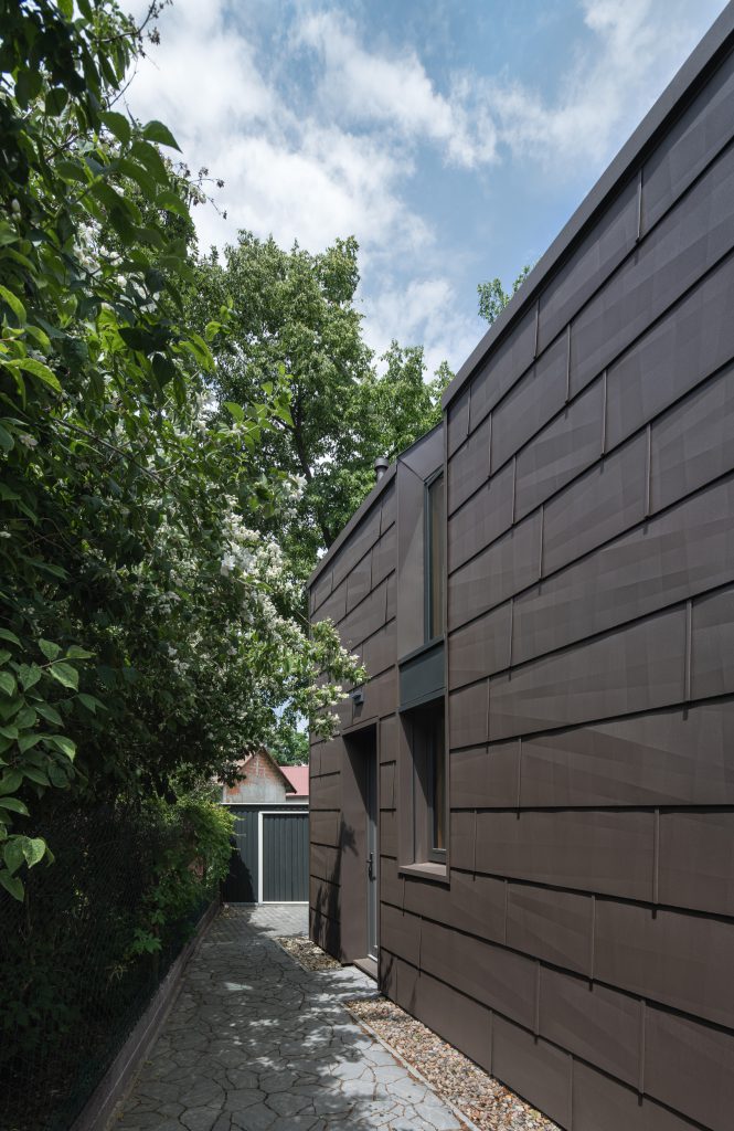 Boční pohled na Lesní chatu, který ukazuje její jednoduchý a přitom elegantní tvar. Zajímavé detaily a propojení s okolními stromy zajišťují přirozenou integraci do krajiny.