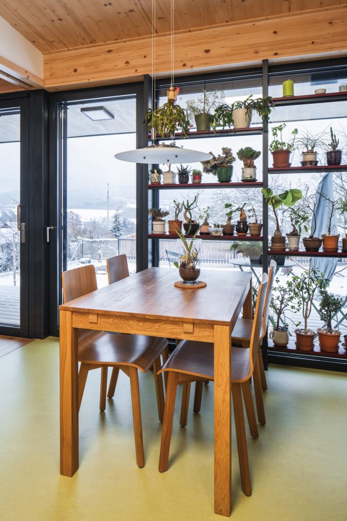 Jídelní kout s dřevěným stolem, přiznaným CLT stropem a velkým prosklením s výhledem ven