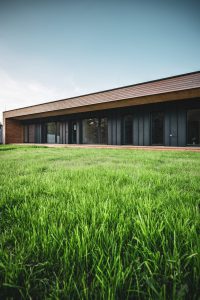 Pohled na přízemní dřevostavbu Housenka s tmavou fasádou a zeleným trávníkem v popředí Další fotku prosím, jsem připraven na pokračování!