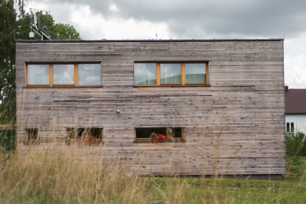 Fasáda dvoupodlažního domu s dřevěným obkladem a okny s rámy