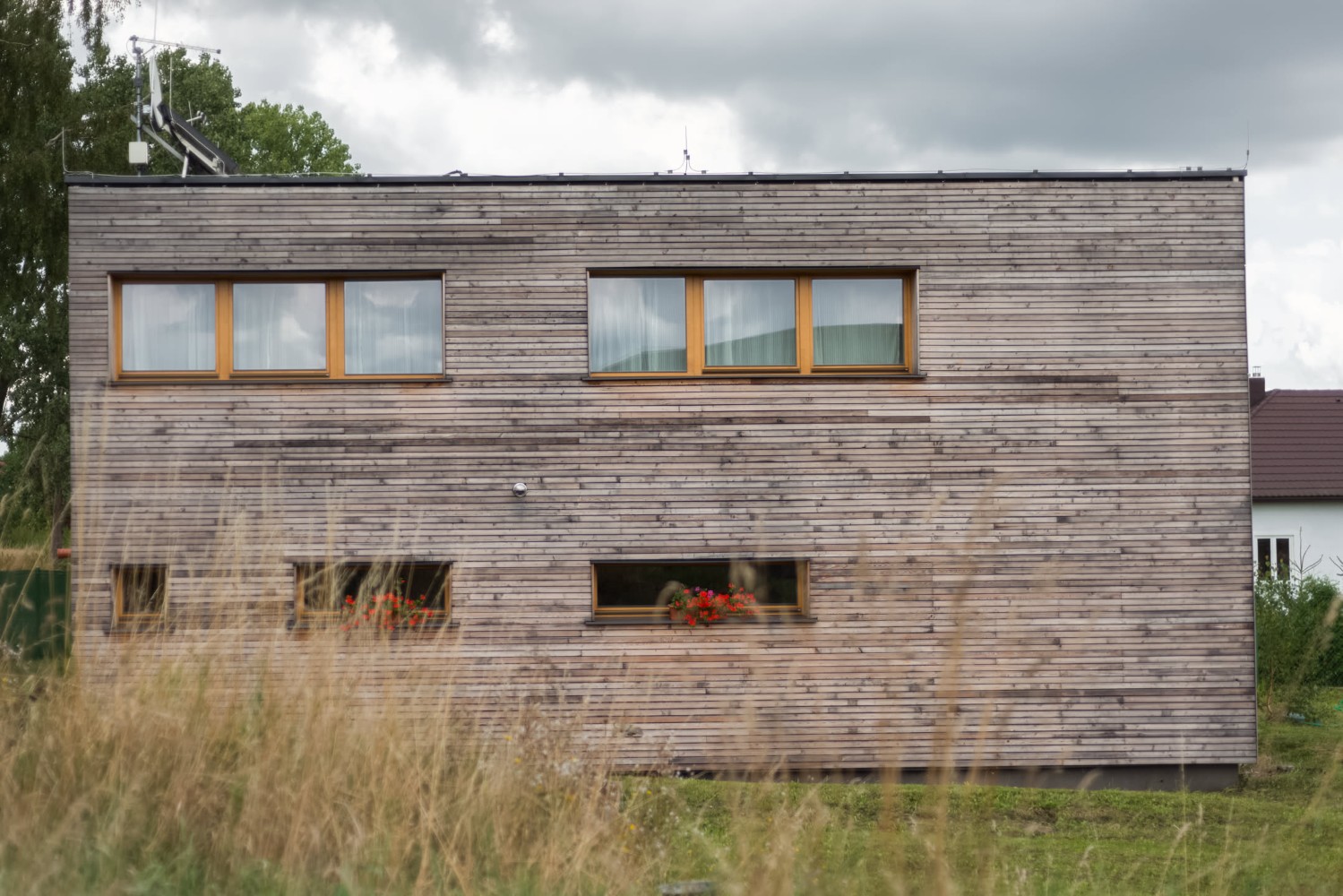 Fasáda dvoupodlažního domu s dřevěným obkladem a okny s rámy