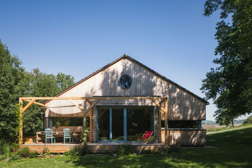 Dům z CLT panelů realizovaný firmou 3AE se sedlovou střechou, dřevěnou terasou a posuvnými dveřmi
