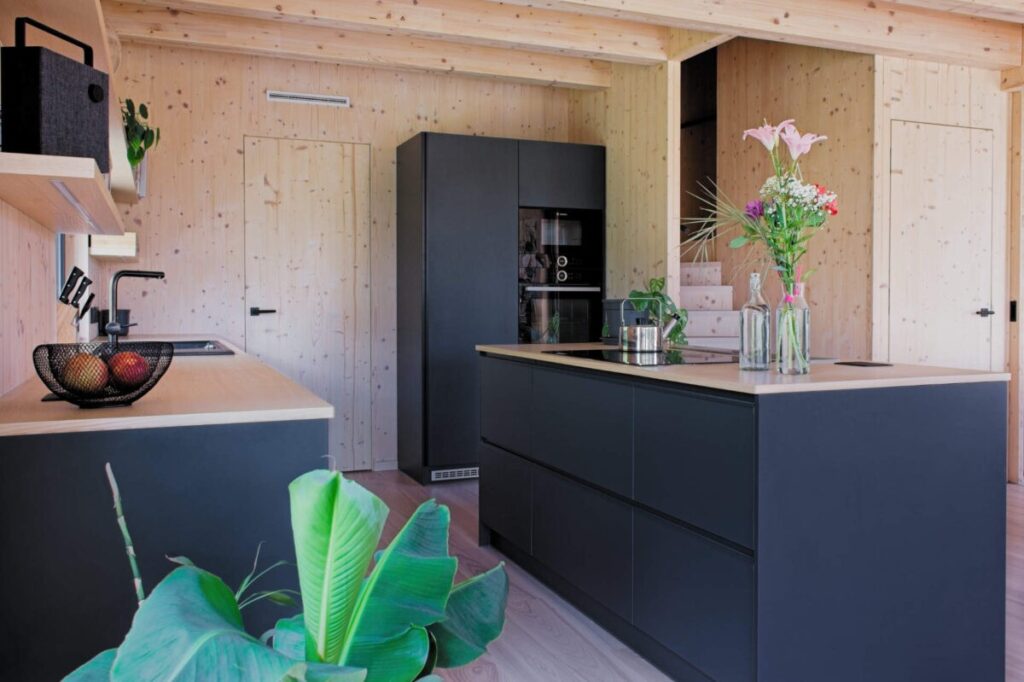 Kuchyňský prostor s černou linkou, ostrůvkem a dřevěnými CLT stěnami