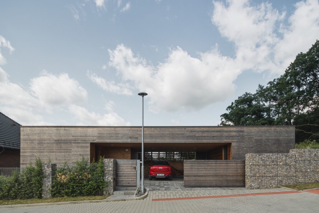 Pohled na vjezd do garáže moderní dřevostavby s dřevěnou fasádou a gabionovým oplocením