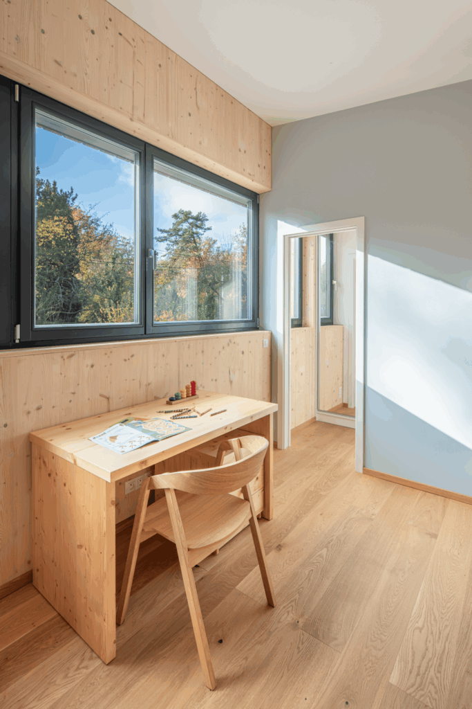 Dětský pokoj s dřevěnými stěnami, psacím stolem a velkými okny