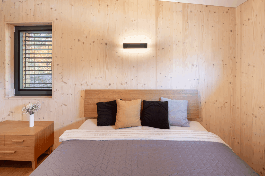 Ložnice s dřevěnými stěnami, postelí a moderními svítidly