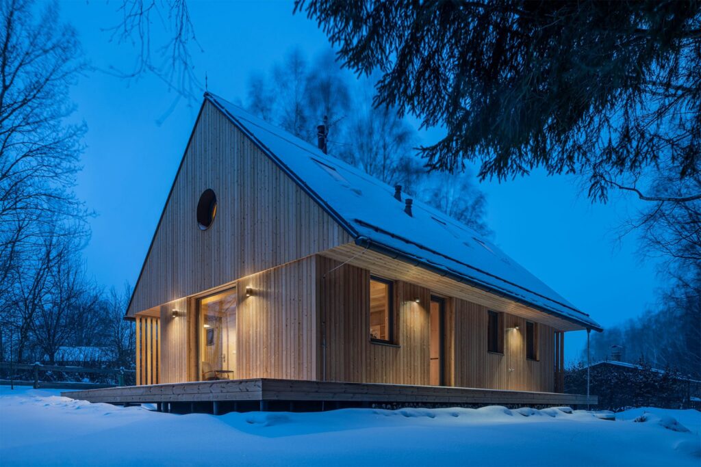 Nasvícená dřevostavba v zimní přírodě s velkým oknem