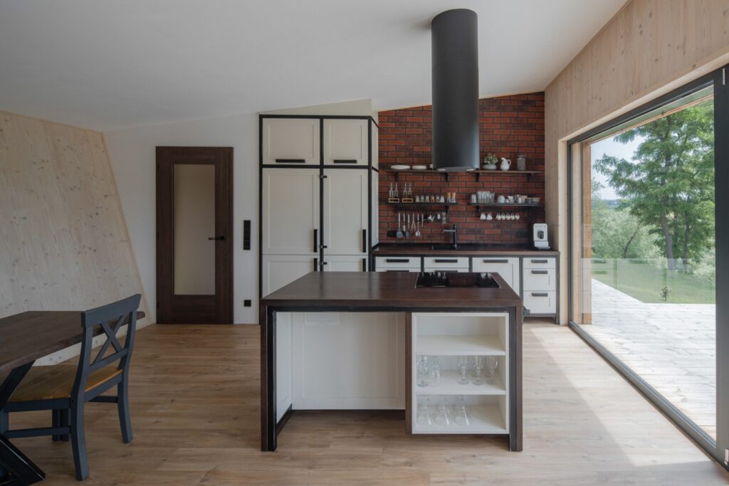 Kuchyně s ostrůvkem, cihlovou stěnou a výhledem do zahrady
