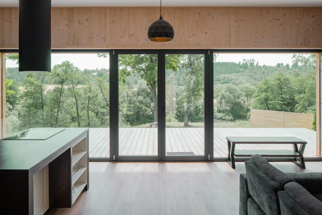 Obývací pokoj s prosklenou stěnou a výhledem na dřevěnou terasu a přírodu