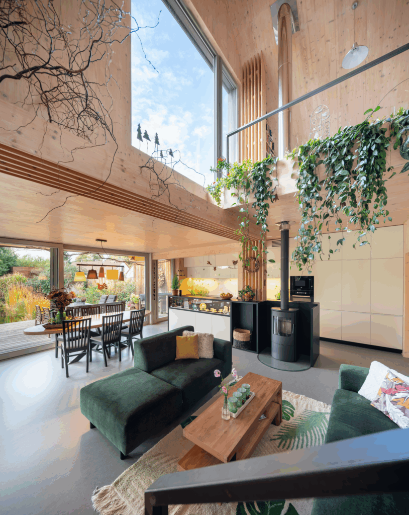 Obývací prostor s vysokým stropem, krbovými kamny a CLT stěnami s výhledem do zahrady