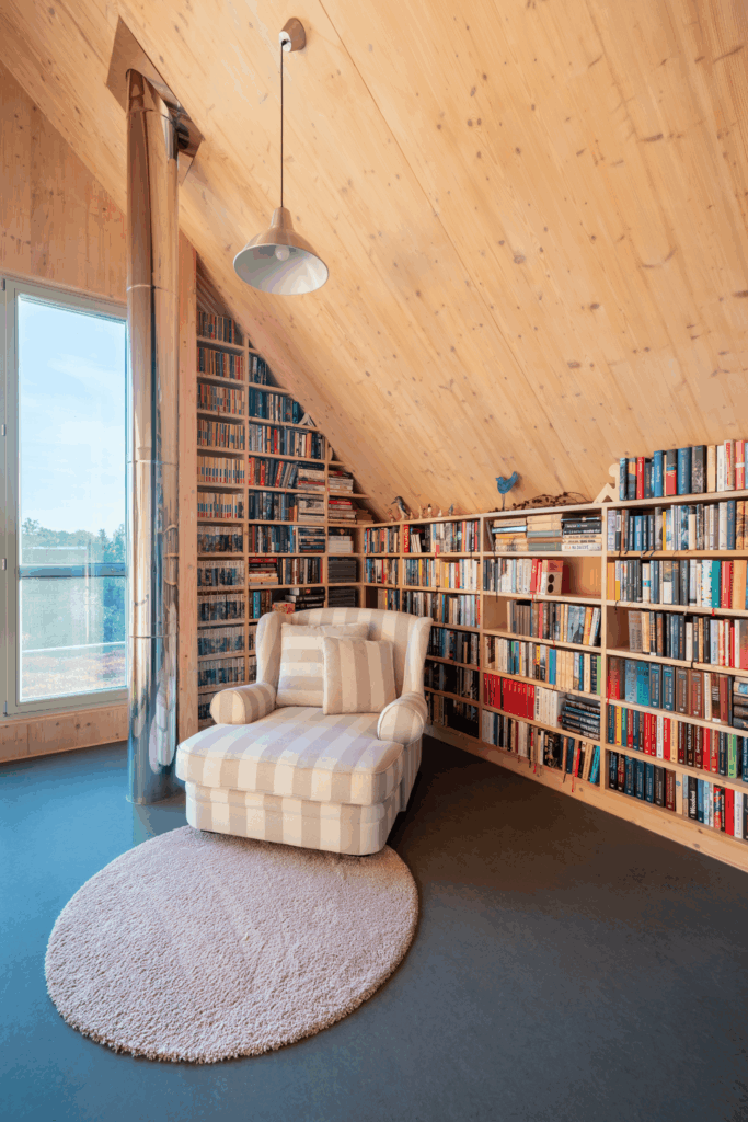 Knihovna v podkroví se šikmým stropem, křeslem a velkým oknem