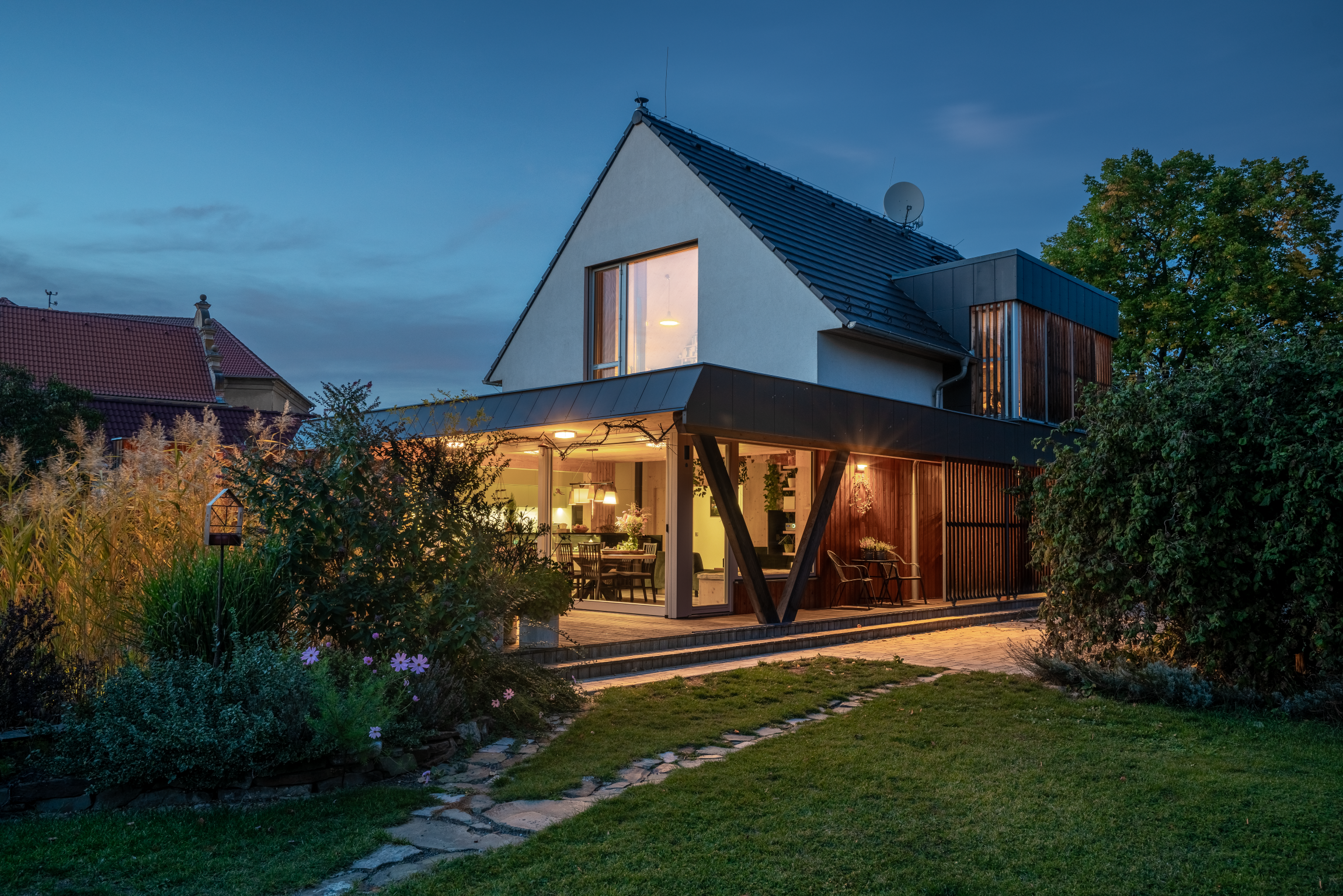 Rodinný dům s krytou terasou, sedlovou střechou a velkými prosklenými plochami směrem do zahrady