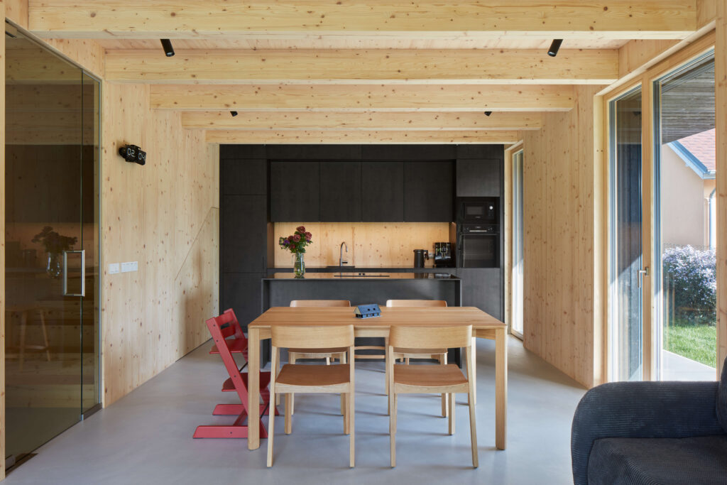 Kuchyň s jídelním stolem, dřevěnými stropy a černou kuchyňskou linkou.