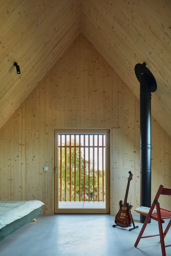 Podkrovní místnost s kamny, kytarou a dřevěným výhledem ven