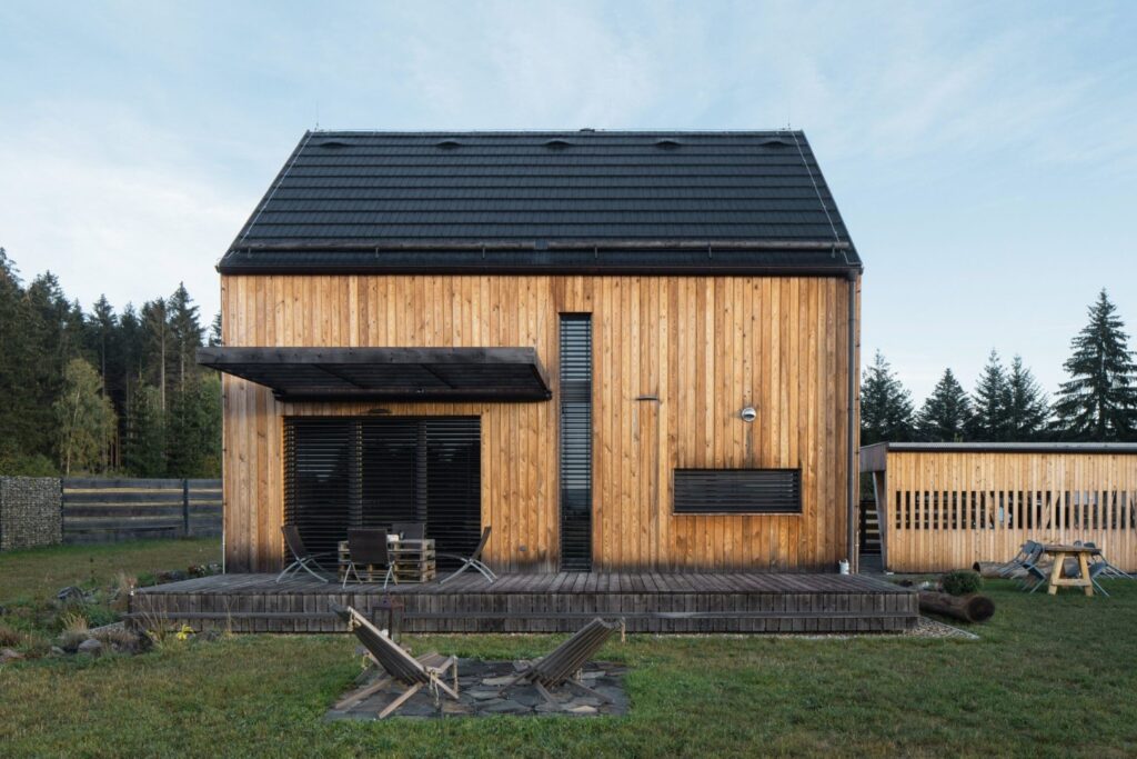 Čelní pohled na dům Kompakt s dřevěnou terasou, vertikálním obkladem a tmavou střechou