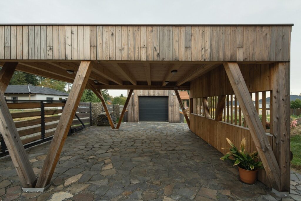 Krytý dřevěný přístřešek s kamennou dlažbou a přístupem ke garáži