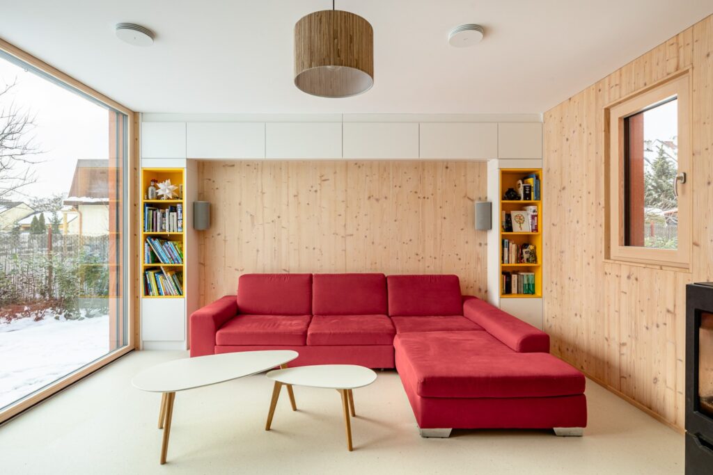 Obývací pokoj s CLT obložením, červenou rohovou sedačkou a výhledem do zasněžené zahrady