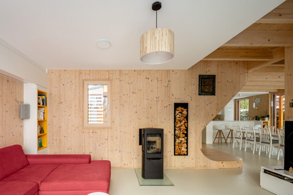 Obývací pokoj s kamny, červenou sedačkou a dřevěným CLT obložením stěn