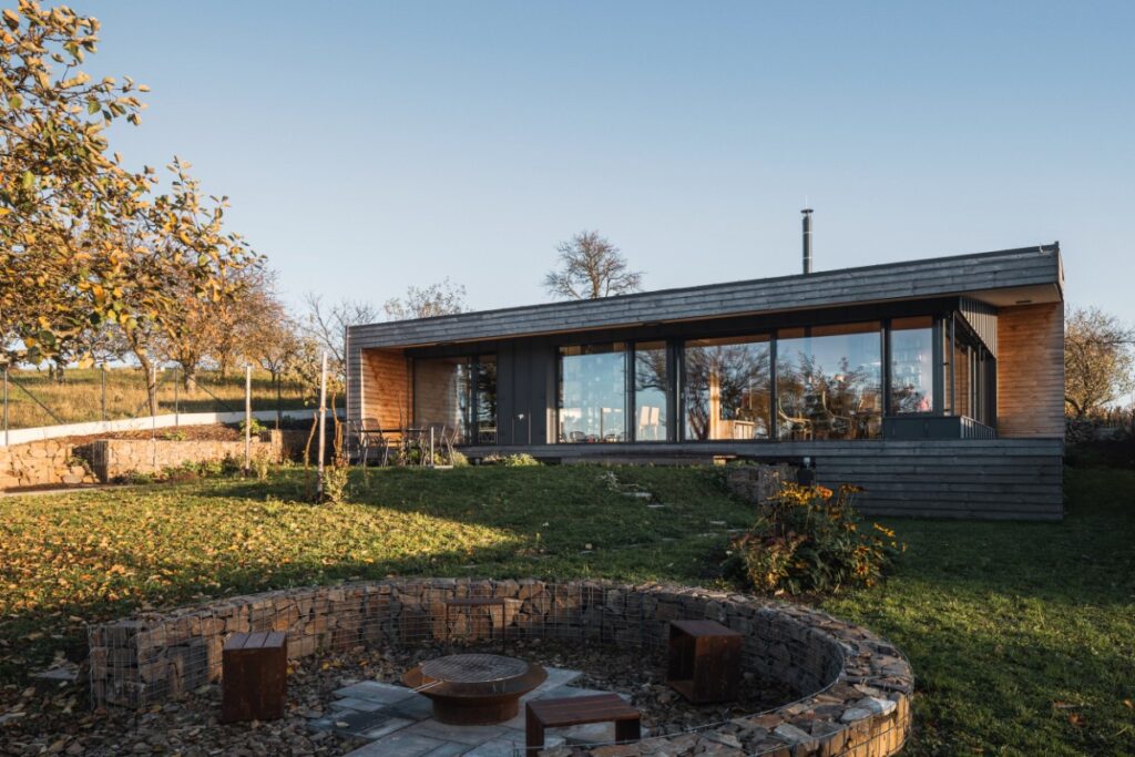 Moderní dřevostavba s prosklením a kamenným ohništěm v zahradě