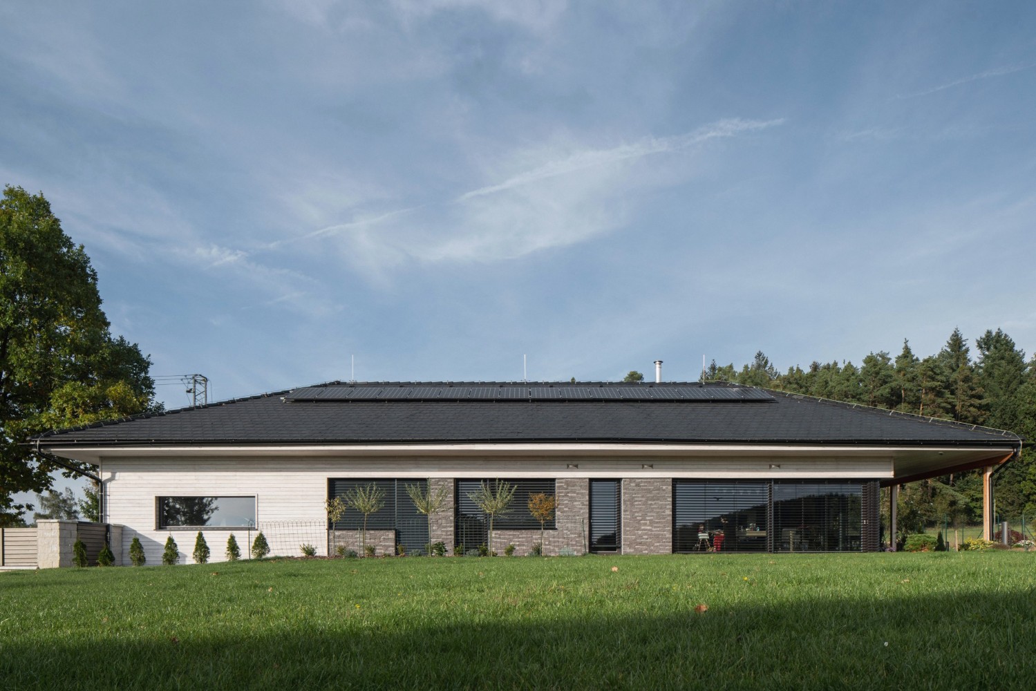 Pohled na nízkoenergetický dům od architekta Lukáše Pejsara od 3ae z CLT panelů s černou střechou, velkými okny a terasou směrem do zahrady