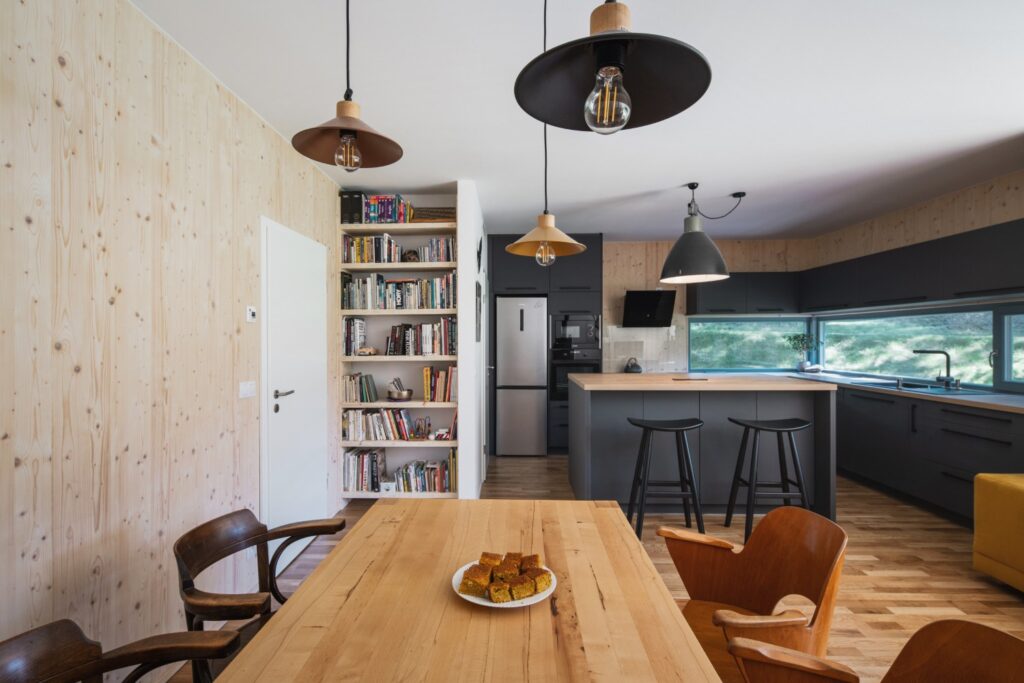 Jídelní kout s dřevěným stolem, kuchyňským ostrůvkem a knihovnou