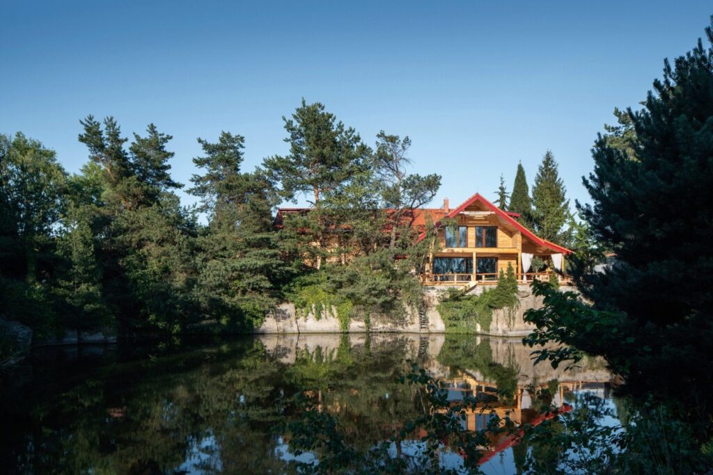 Dům ze dřeva ve stylu chaletu postavený nad zatopeným lomem obklopený stromy