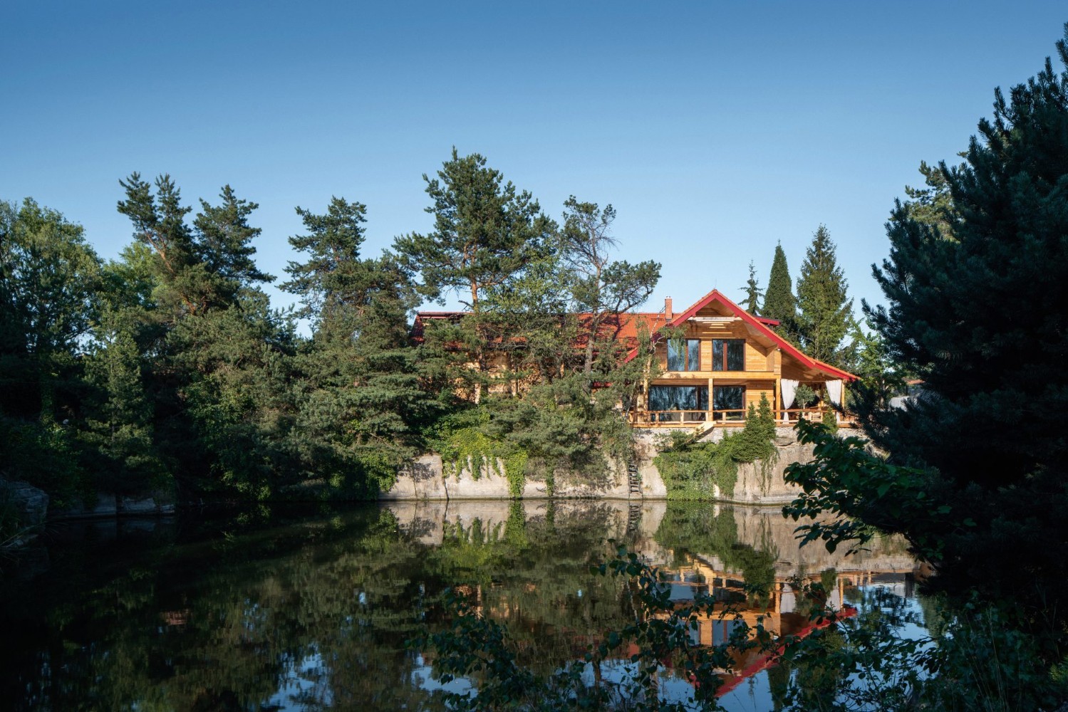 Dům ze dřeva ve stylu chaletu postavený nad zatopeným lomem obklopený stromy