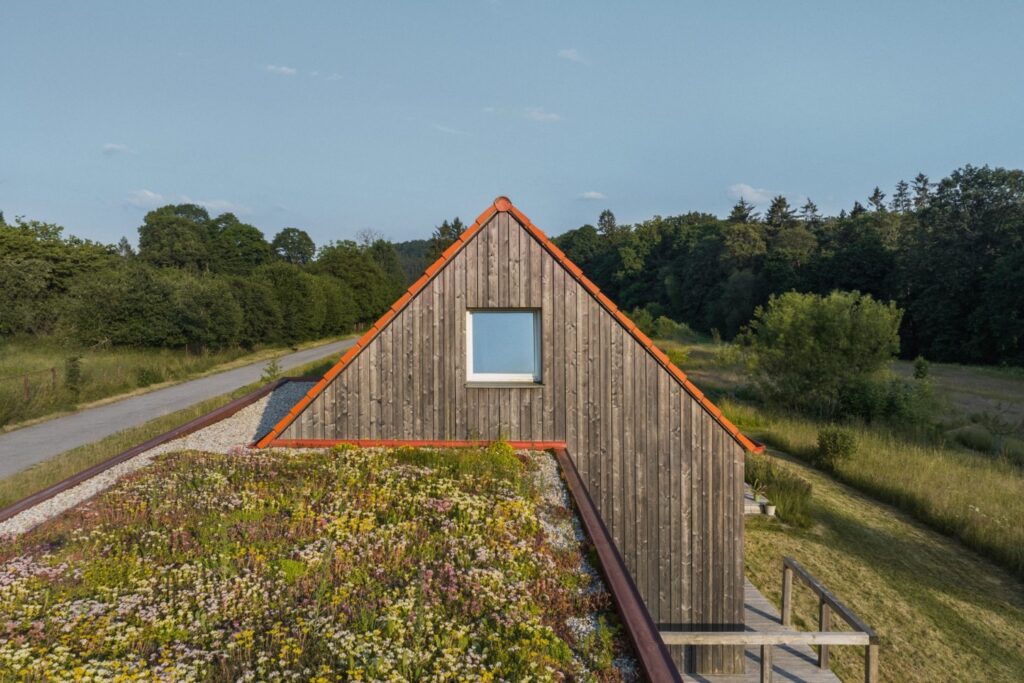 Dřevostavba 3AE s dřevěným štítem a zelenou střechou u venkovské cesty