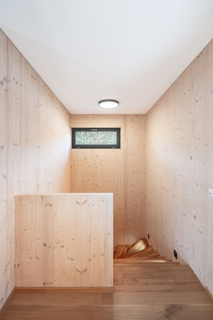 Schodiště s dřevěnými stěnami a malým oknem v interiéru dřevostavby
