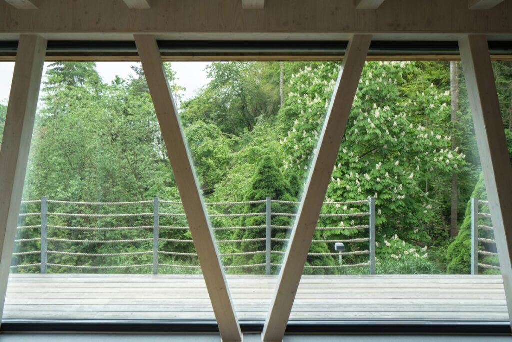 Obývací prostor s velkými okny, výhledem do lesa a přiznanými trámy