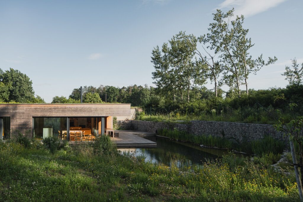 CLT dřevostavba s dřevěnou fasádou a jezírkem u terasy v přírodní zahradě
