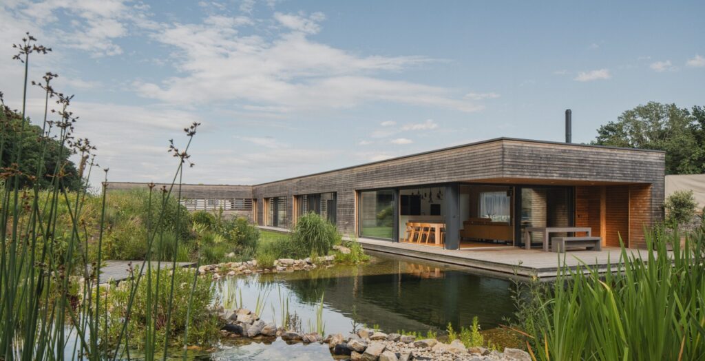 Přízemní vila nad vodou ve tvaru L s dřevěnou fasádou a jezírkem u terasy