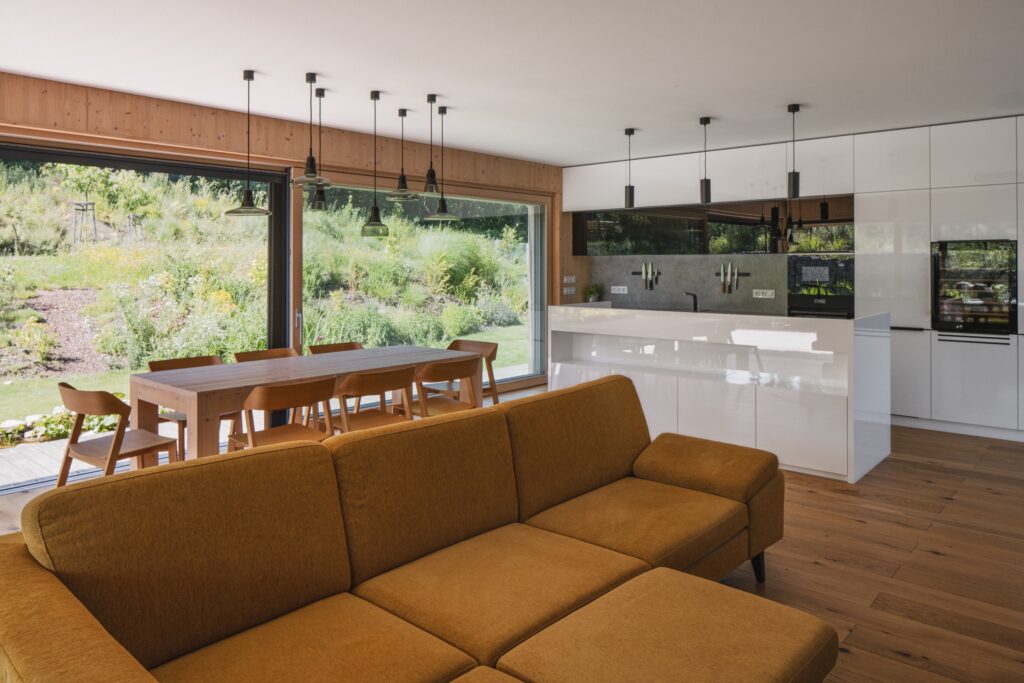 Moderní interiér s kuchyní, jídelním stolem a výhledem na zahradu přes prosklenou stěnu