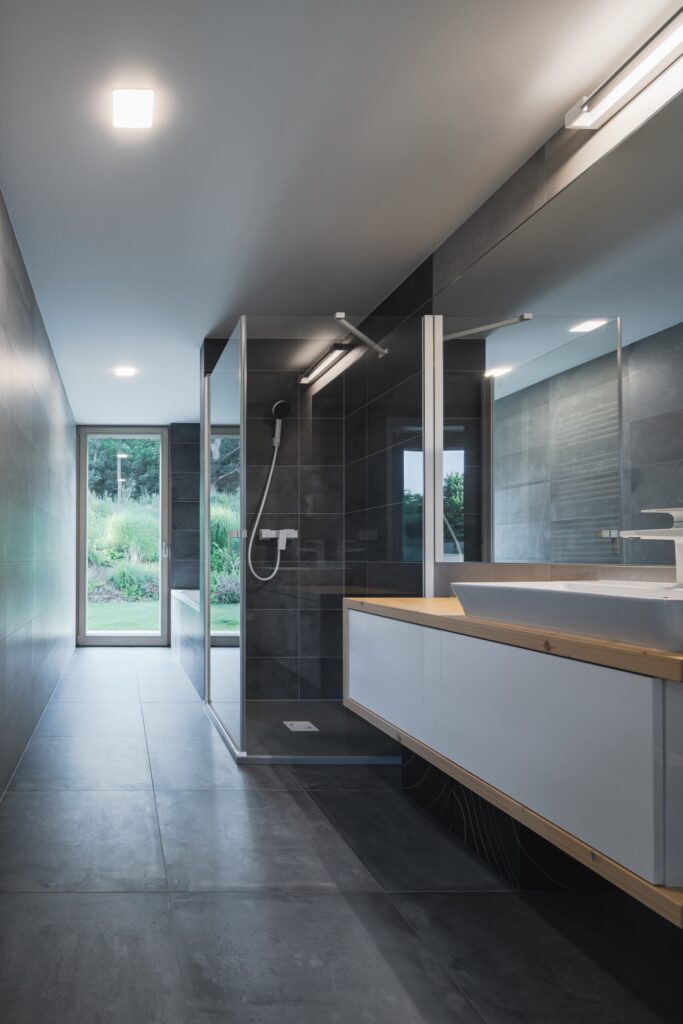 Moderní koupelna s černou dlažbou, walk-in sprchou a výhledem do zahrady