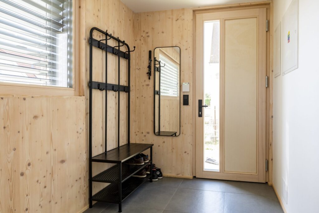 Zádveří dřevostavby s CLT obkladem, věšákem, zrcadlem a vstupními dveřmi