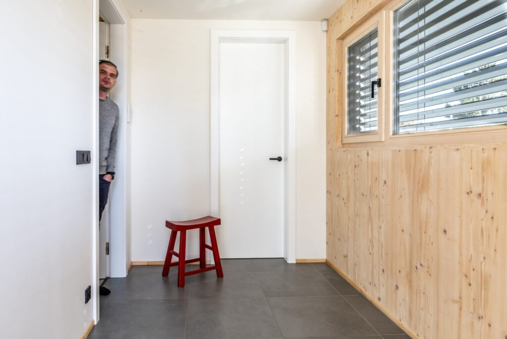 Chodba v dřevostavbě s dřevěným obkladem, bílými dveřmi a červenou stoličkou