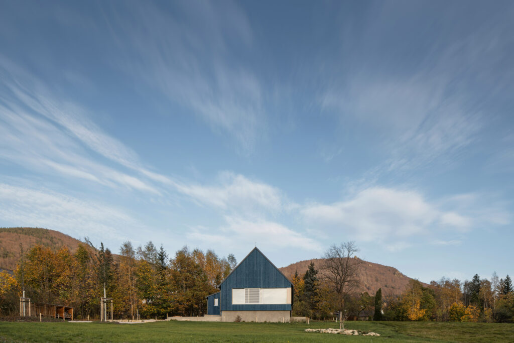 Chata s trojúhelníkovým štítem, modrou fasádou a betonovým soklem