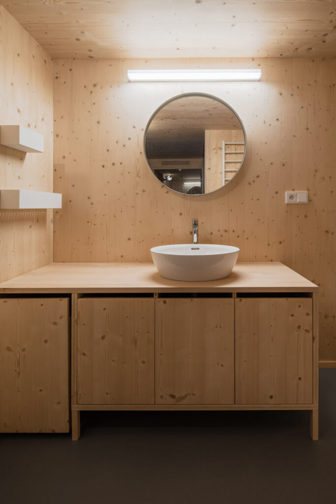 Umyvadlo na dřevěné skříňce s kulatým zrcadlem v CLT koupelně