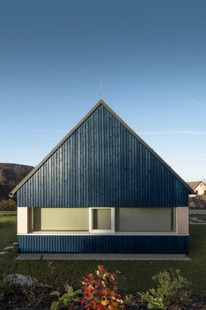 Přední fasáda chaty s modrým obkladem a velkým horizontálním oknem