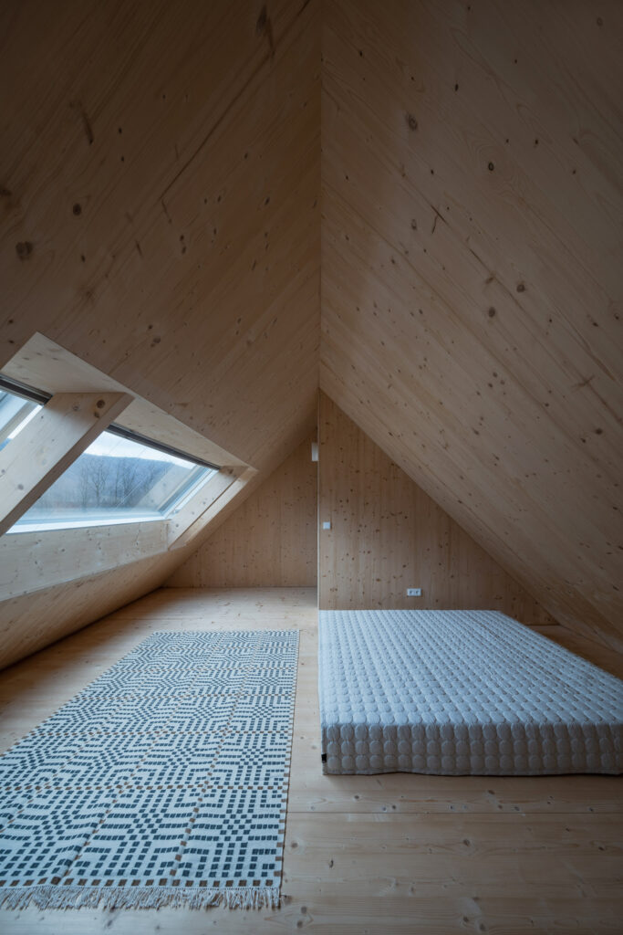 Podkrovní ložnice s matrací a střešním oknem v CLT interiéru