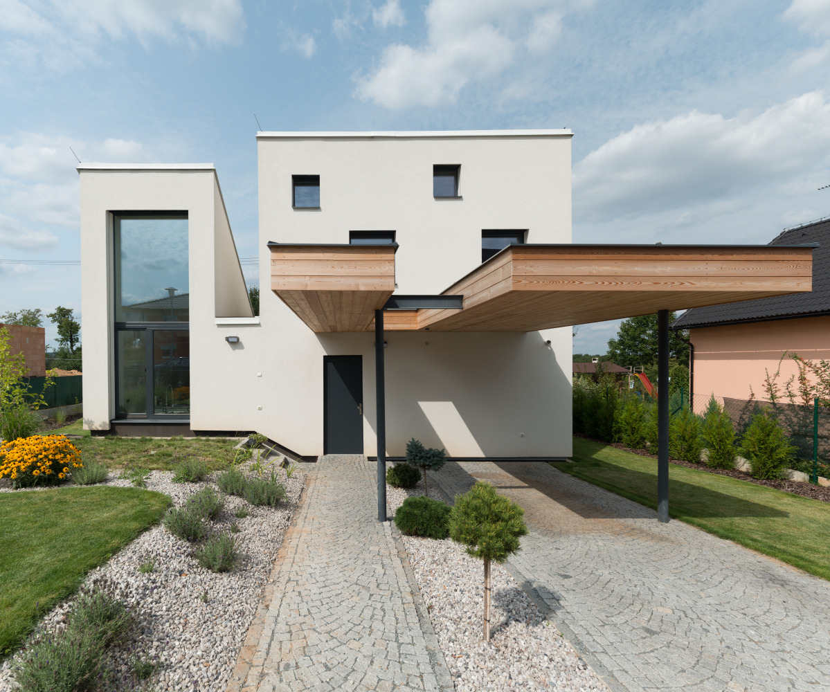 Čelní pohled na dřevostavbu s plochou střechou a dřevěným přístřeškem pro auto