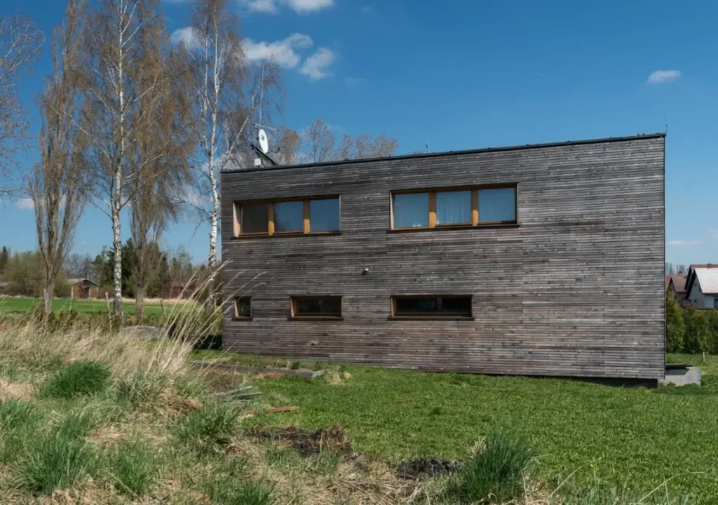 Realizace moderní dvoupodlažní dřevostavby 3AE s tmavým vodorovným obkladem a plochou střechou.