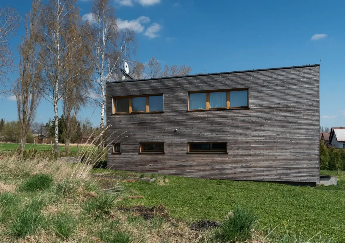 Realizace moderní dvoupodlažní dřevostavby 3AE s tmavým vodorovným obkladem a plochou střechou.