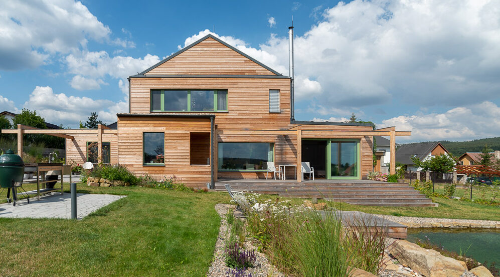 Moderní dřevostavba s dřevěnou fasádou, terasou a jezírkem na zahradě